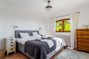 A bedroom with a bed, nightstands, a dresser, a window with curtains, and a ceiling light. - Villa Virettes – Peaceful haven with pool (Tourrettes-sur-Loup)