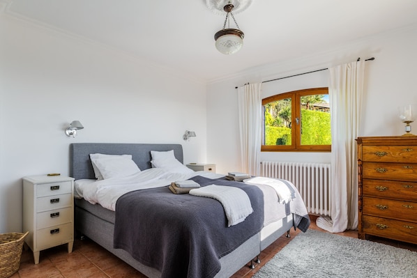 A bedroom with a bed, nightstands, a dresser, a window with curtains, and a ceiling light.