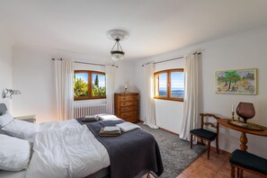 A bedroom with a bed, a dresser, a chair, a table, and a painting.