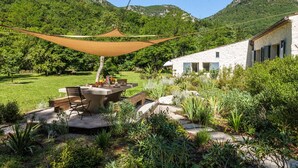 A patio with a table and chairs, surrounded by lush greenery and a mountain backdrop. - Villa Health – River & pool by Gorges du Loup (Tourrettes-sur-Loup)
