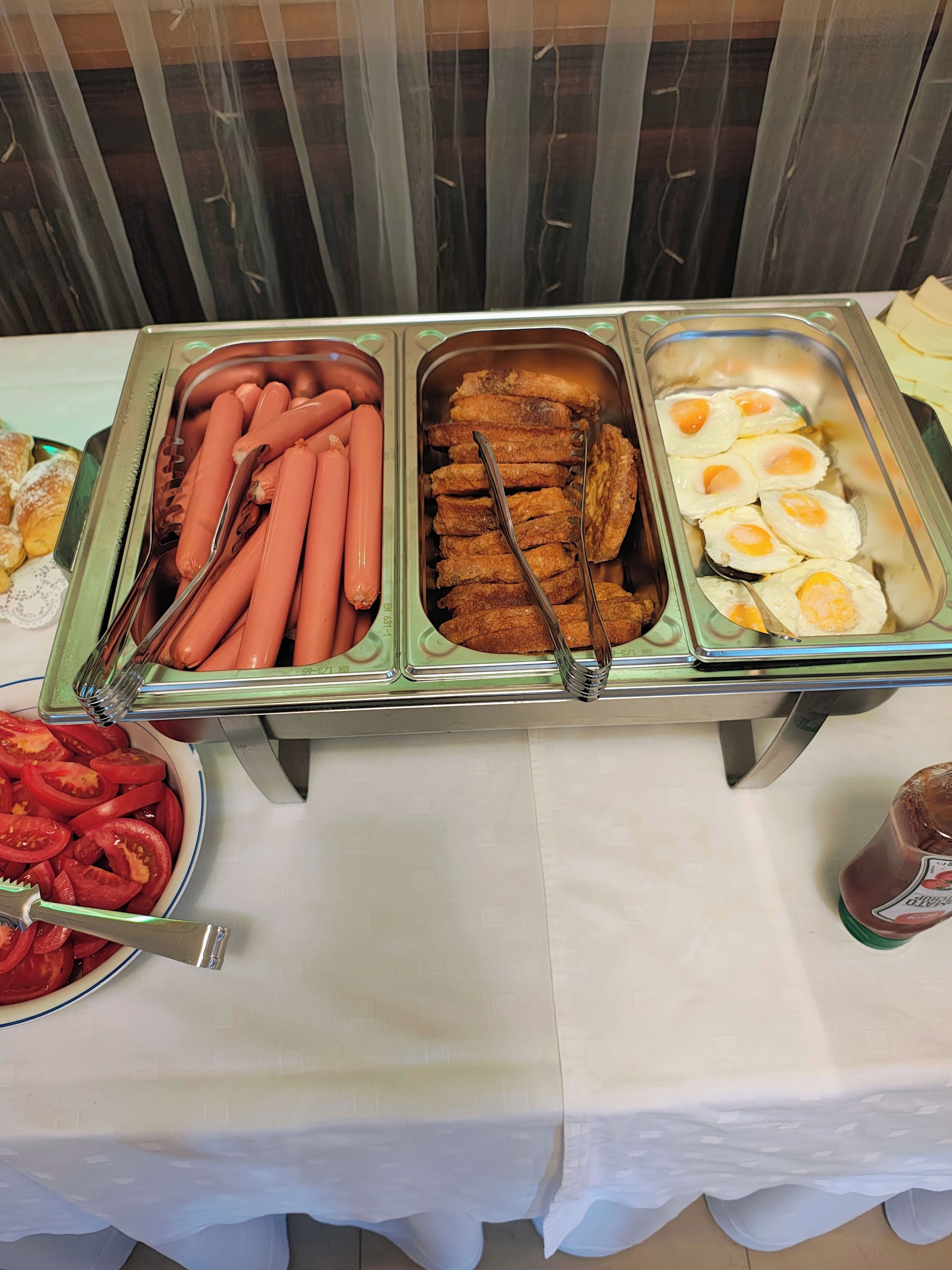 Una mesa de buffet con bandejas de salchichas, pollo frito y huevos fritos.