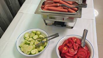 Una mesa de bufé con distintos alimentos, incluyendo hot dogs, pepinos en rodajas y tomates.