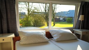 A bedroom with a bed, two pillows, a bedside table, a lamp, and a window with a view of greenery and a house. - Vacation home with terrace in Bruinisse near Renesse for up to 6 people (Bruinisse)