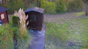 A wooden cabin with a stone pathway leading to it, surrounded by lush greenery and pampas grass. - Vacation home with terrace in Bruinisse near Renesse for up to 6 people (Bruinisse)