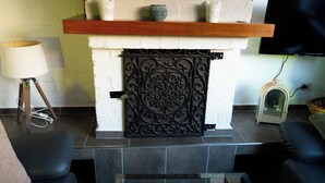 A fireplace with a decorative metal door, a wooden shelf above it, and a flat-screen TV mounted on the wall. - Vacation home with terrace in Bruinisse near Renesse for up to 6 people (Bruinisse)
