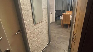 A hallway with a white brick wall, a door with a handle, and a mirror. There is a dining area with a table and chairs visible through an open door. - Vacation home with terrace in Bruinisse near Renesse for up to 6 people (Bruinisse)