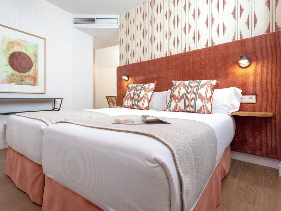 Una habitación de hotel moderna con una cama grande, un cabecero con diseño estampado, una lámpara fijada a la pared y una obra de arte enmarcada sobre la cama.