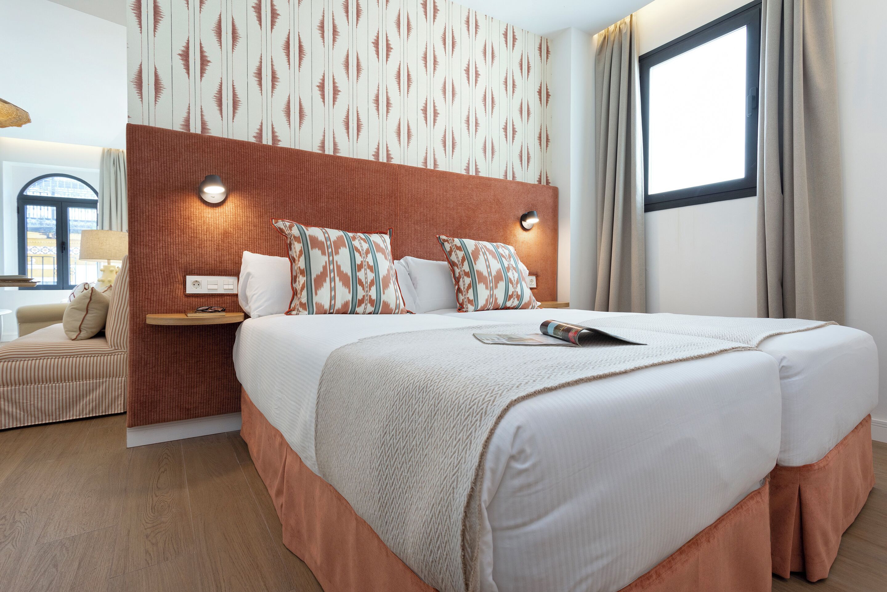 A hotel room with a large bed, a bedside table, a lamp, and a window with curtains.