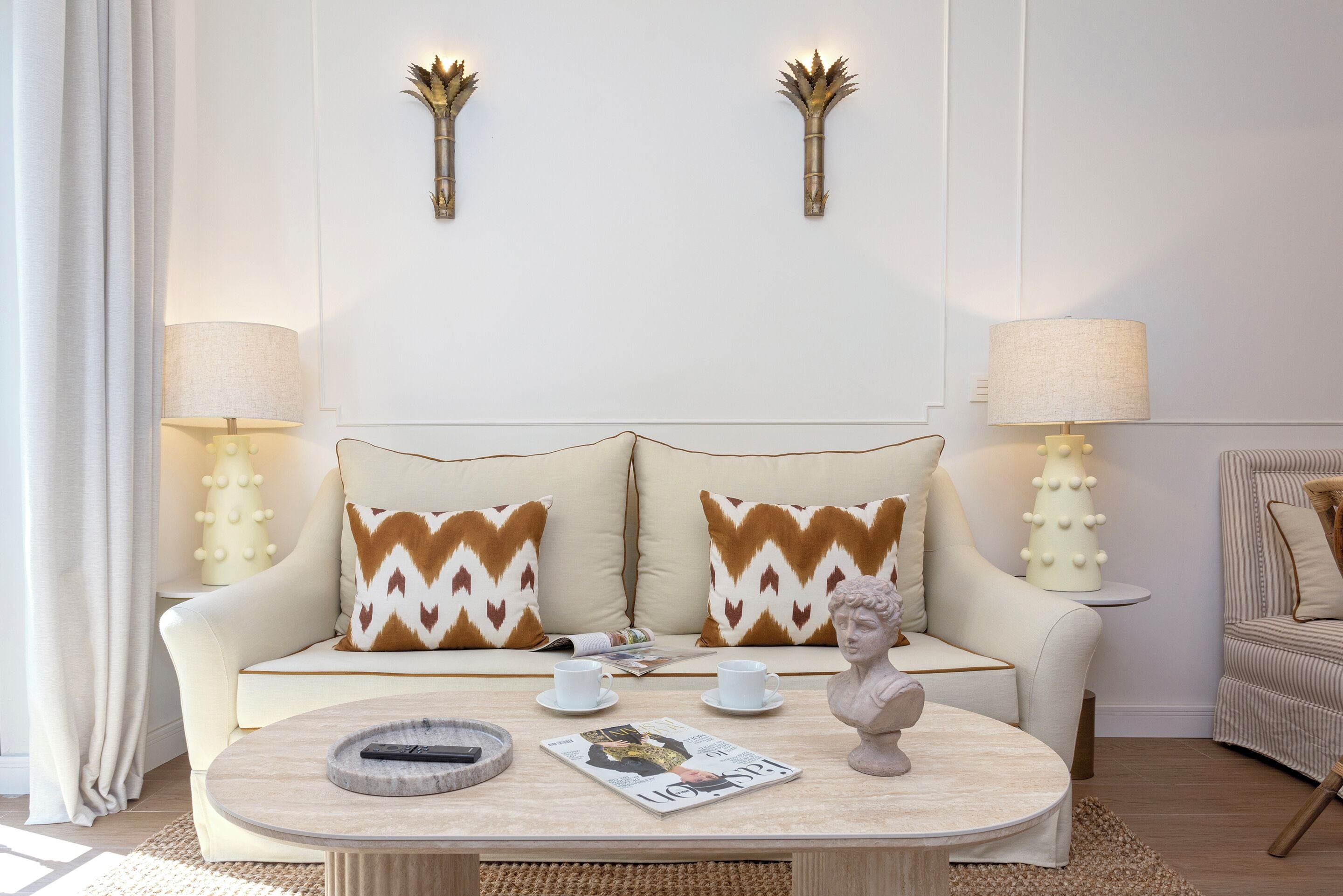 Una sala de estar moderna con un sofá, dos luces decorativas fijadas a la pared, una mesa de centro con una revista, tazas y un control remoto.