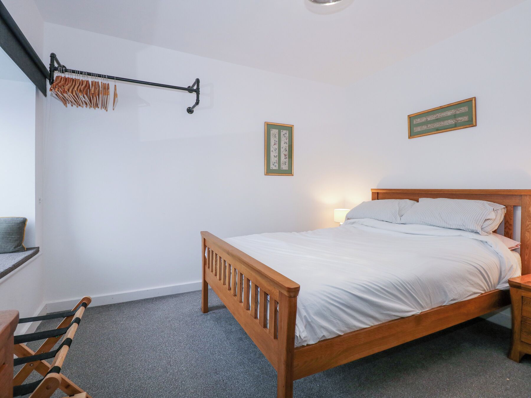 Een slaapkamer met een houten bed, een nachtkastje, een wandrek met hangende spullen, en twee ingekaderde foto's.