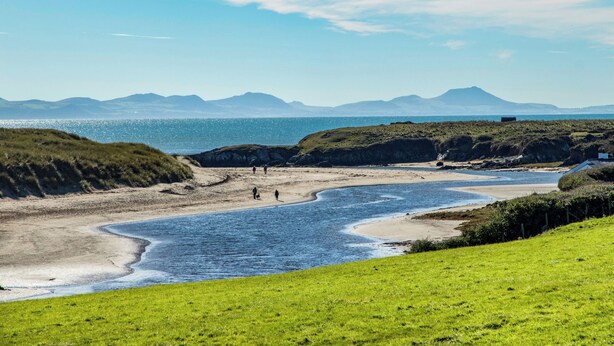 Un paisaje costero con una playa, zonas verdes y montañas a lo lejos.
