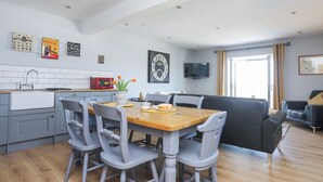 Una cocina moderna con comedor, que incluye una mesa de madera, sillas grises, un microondas rojo y un reloj en la pared.