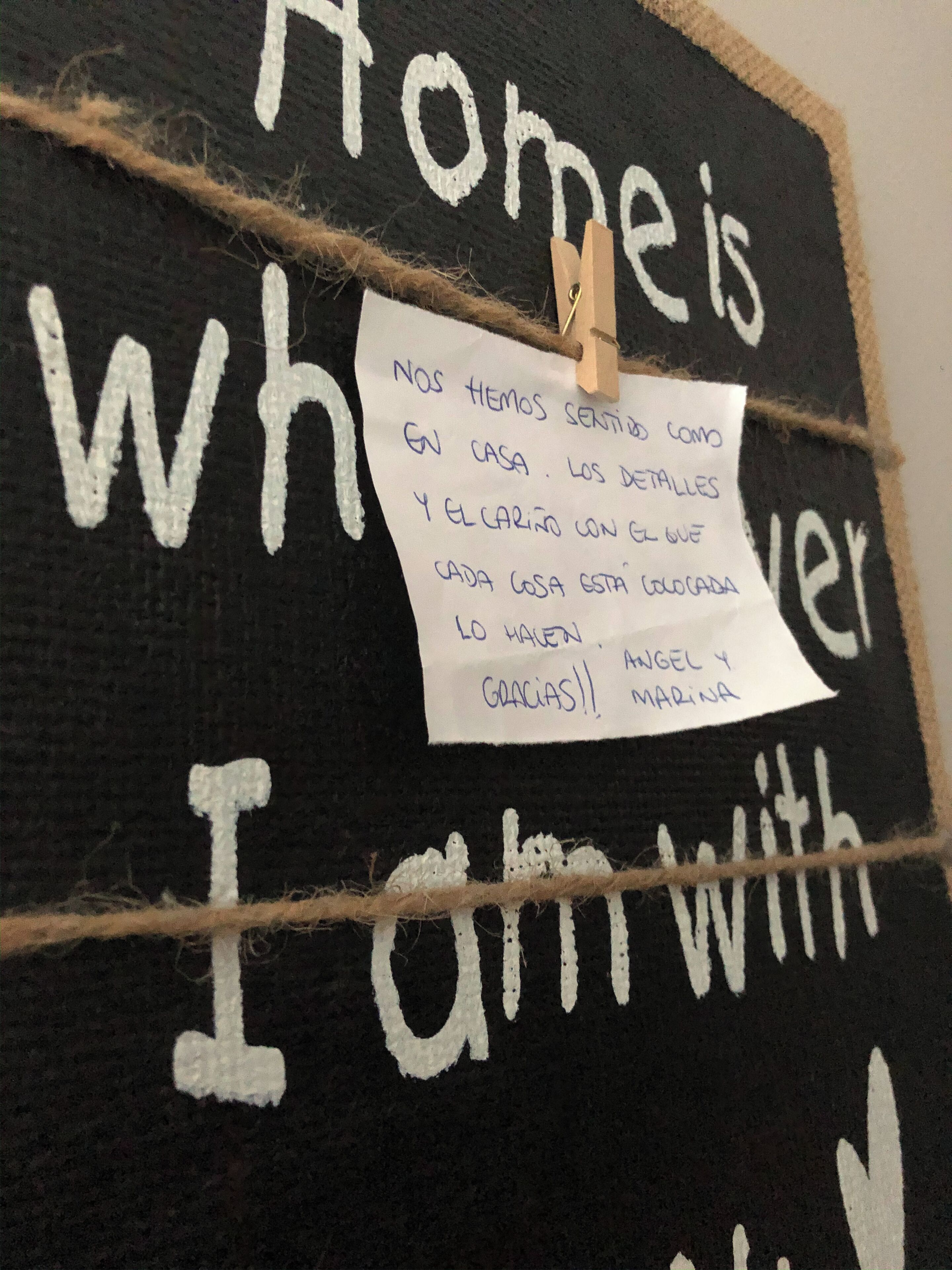 A blackboard with white text saying "Home is where I am with" and a handwritten note attached.