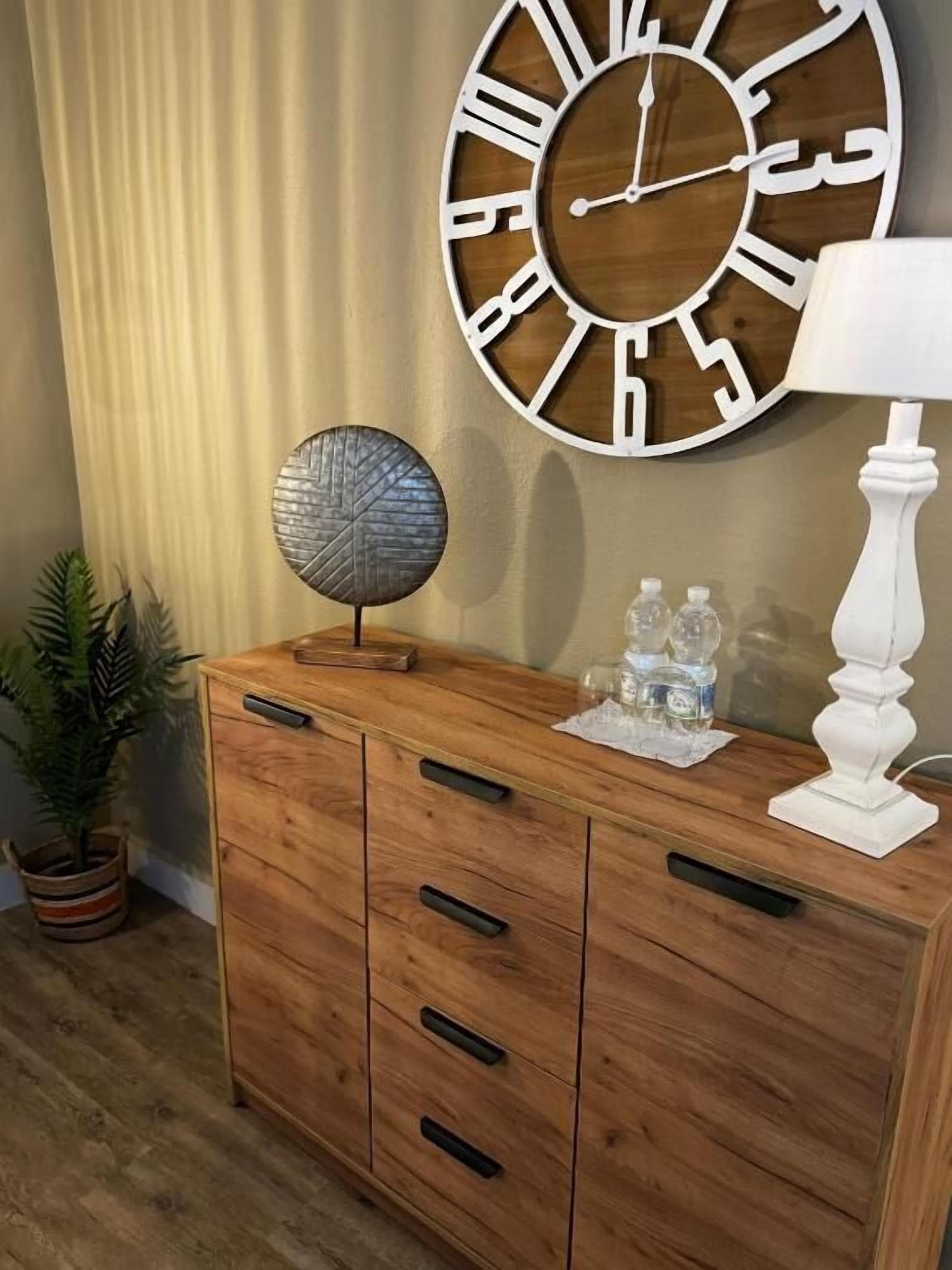 Un mueble de madera con cajones, un reloj de pared redondo, un globo decorativo, una lámpara blanca y una planta en maceta.