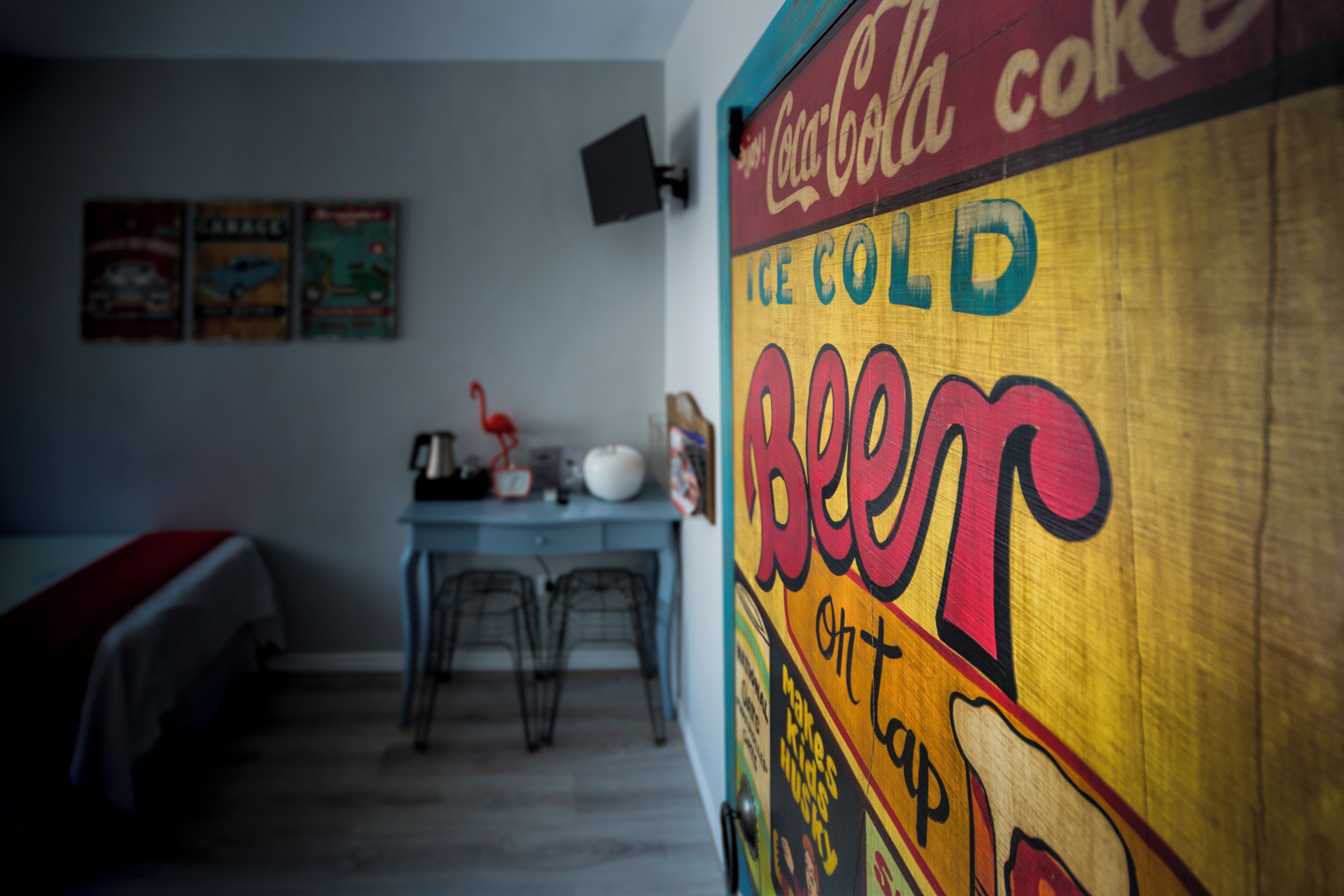 Una habitación con una cama, un escritorio y un cartel de Coca-Cola Ice Cold Beet en la pared.