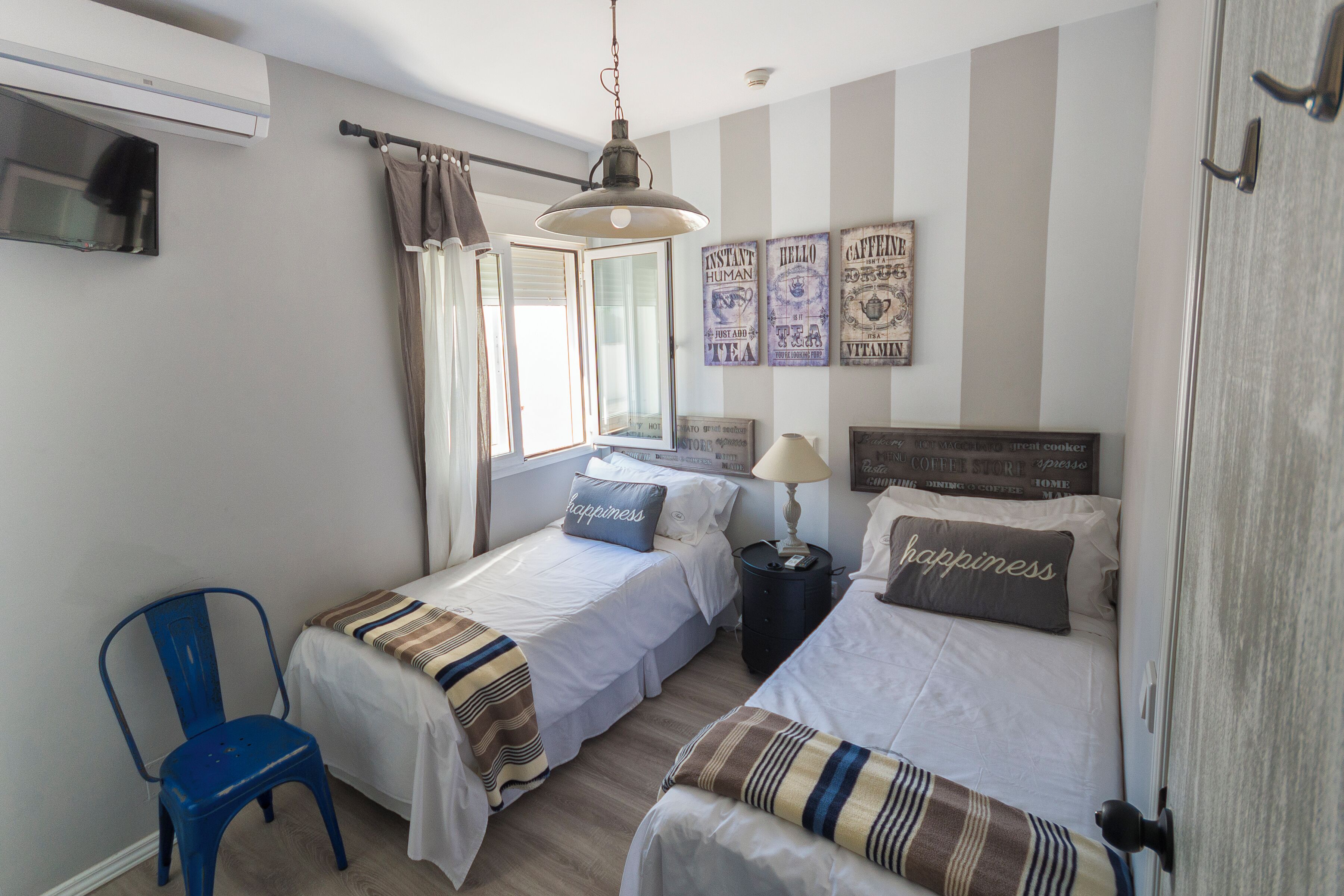 A bedroom with two beds, a chair, a lamp, and wall art.