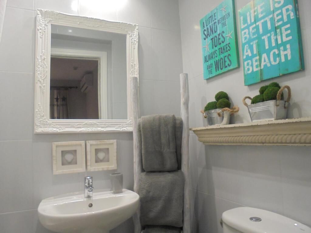 Une salle de bain avec un lavabo blanc, un miroir doté d’un cadre orné et deux panneaux muraux affichant des citations inspirantes.