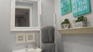 Une salle de bain avec un lavabo blanc, un miroir doté d’un cadre orné et deux panneaux muraux affichant des citations inspirantes.