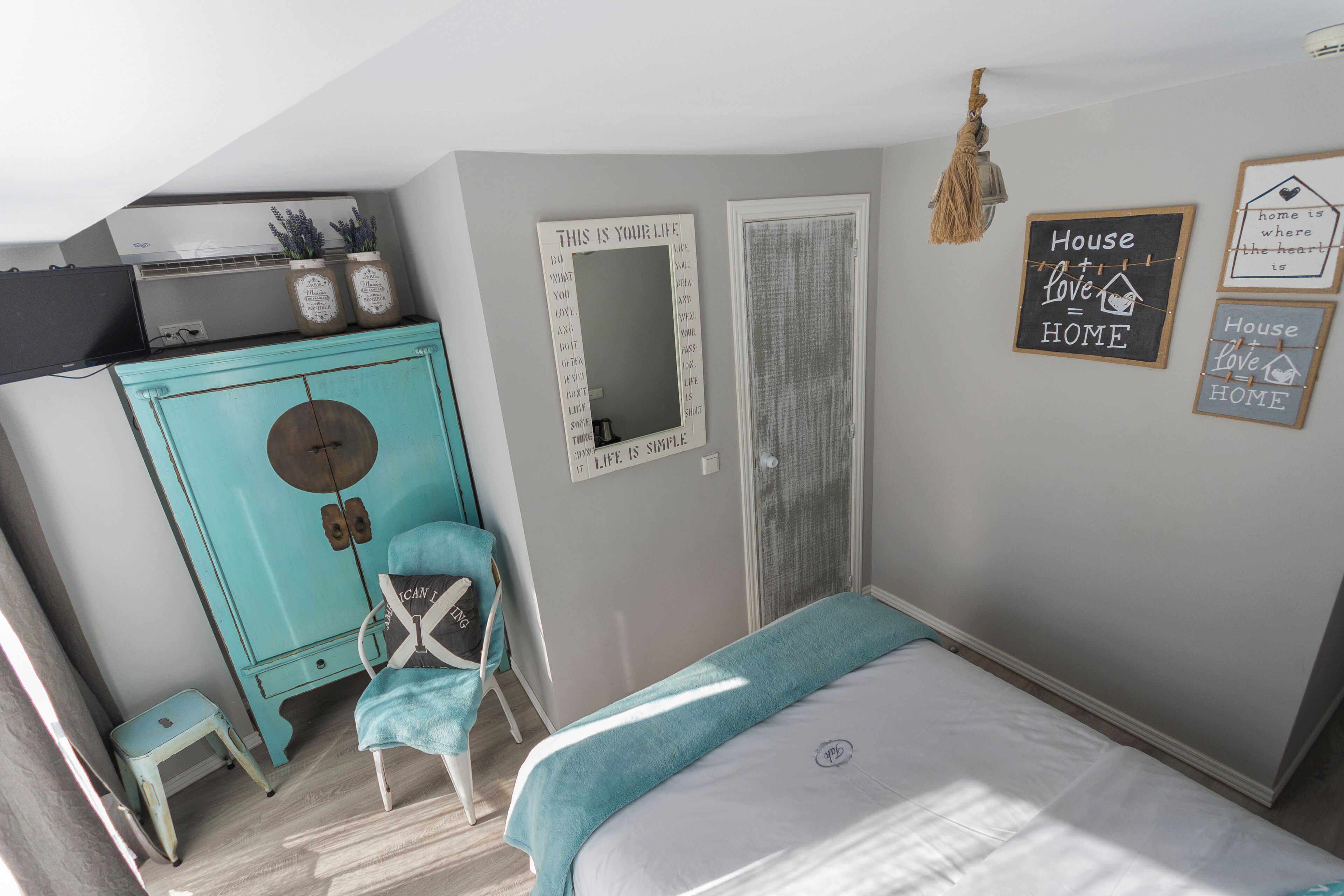 A bedroom with a bed, a turquoise dresser, a chair, and motivational wall art.