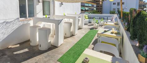 An outdoor seating area with white furniture, a green artificial turf path, and a stone centerpiece on a table.