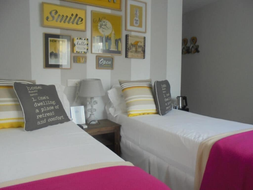 Une chambre d’hôtel avec deux lits, une table de chevet, une lampe et des éléments de décoration murale, notamment des tableaux encadrés et un panneau sur lequel est écrit « Souriez ».