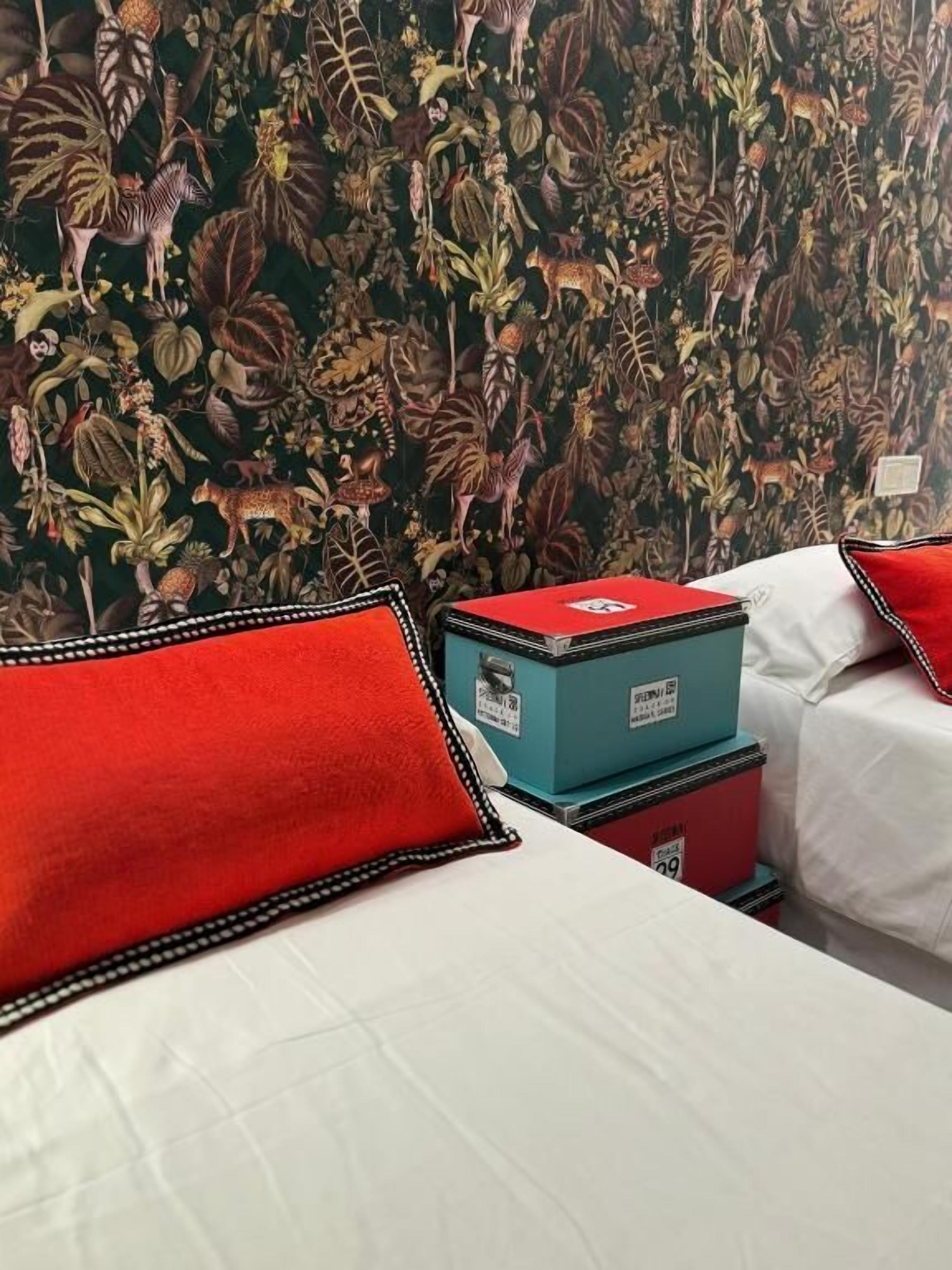 A hotel room with a bed, pillows, and a wall with a dense jungle-themed wallpaper.