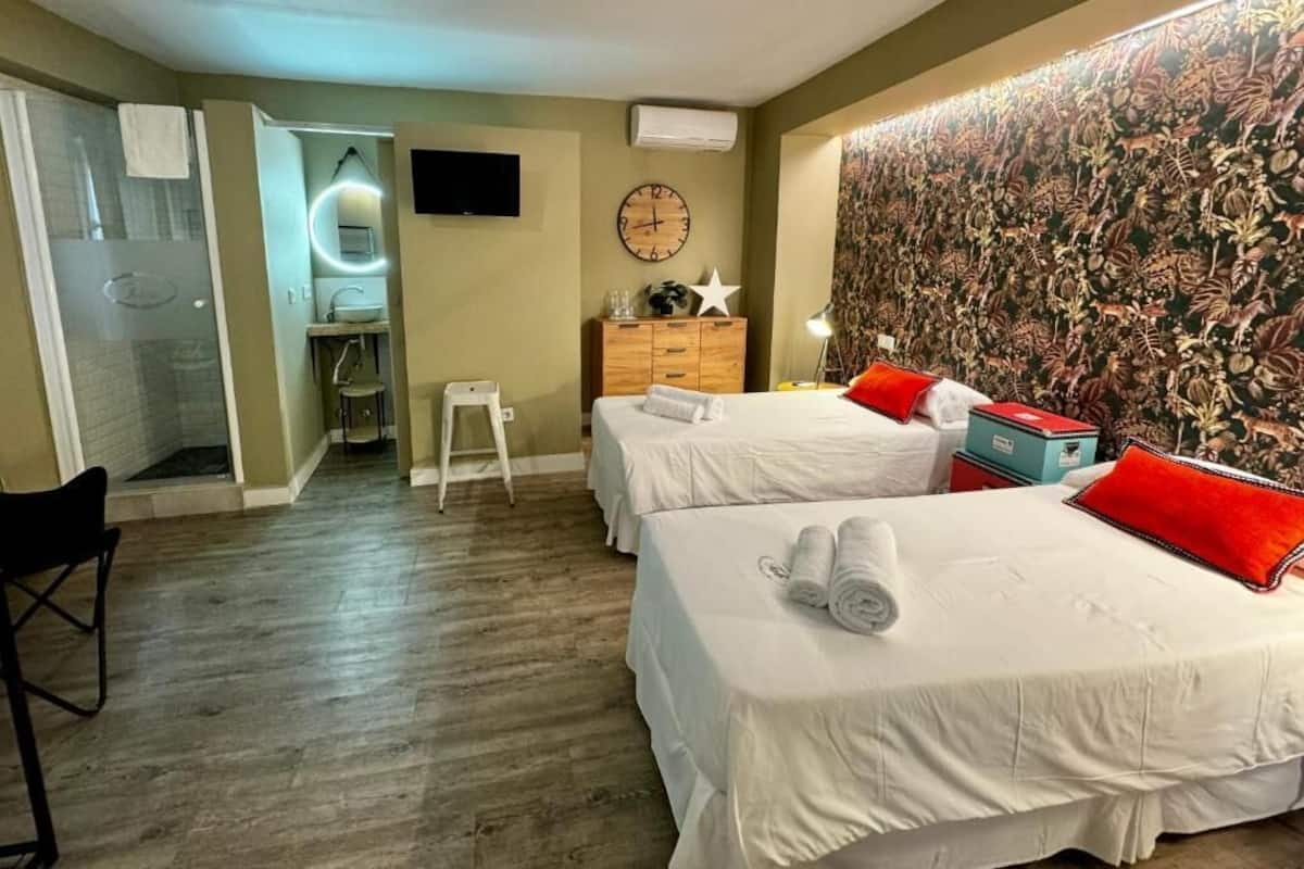 Habitación de hotel con dos camas, un aparador de madera, un televisor, un reloj y un papel tapiz estampado.