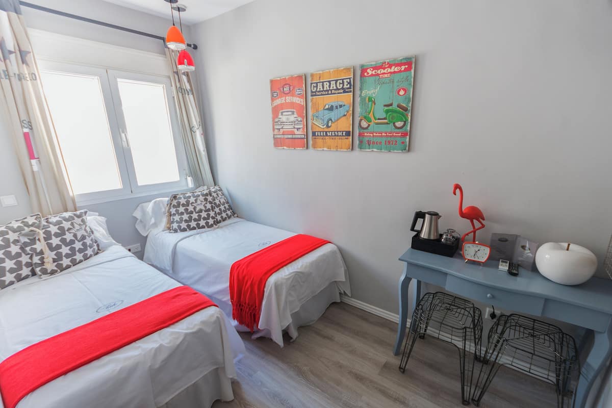 Un dormitorio con dos camas, una ventana con cortinas, un escritorio con lámpara y decoración en la pared.
