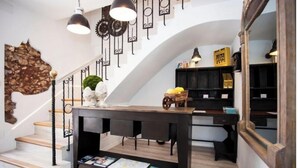 Una escalera con detalles de madera y barandillas negras que conduce a una habitación con una mesa de madera oscura, libros y objetos decorativos.