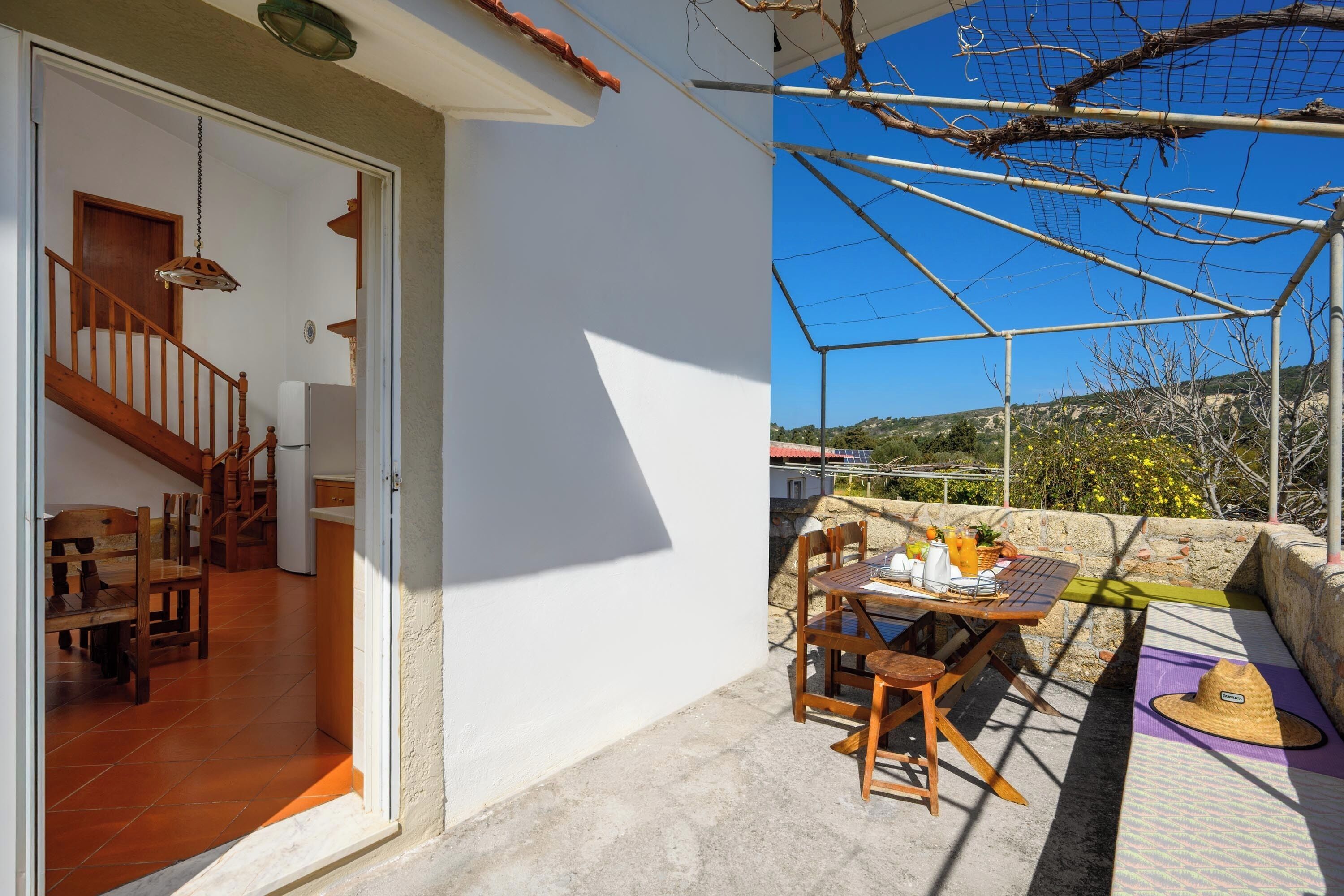 A patio with a table and chairs, a hat, and a view of the countryside.