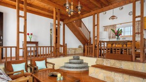 A spacious living area with a wooden staircase, a stone fireplace, and a dining table. - Yanni’s Place (93MF+669 Petaloudes, Greece)