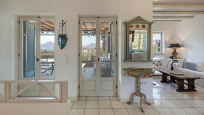 A room with a view of a mountain, a white sofa, a small table, and a decorative mirror. - Isterni | 3BR Sea View House | Coral Pearl (Paros)