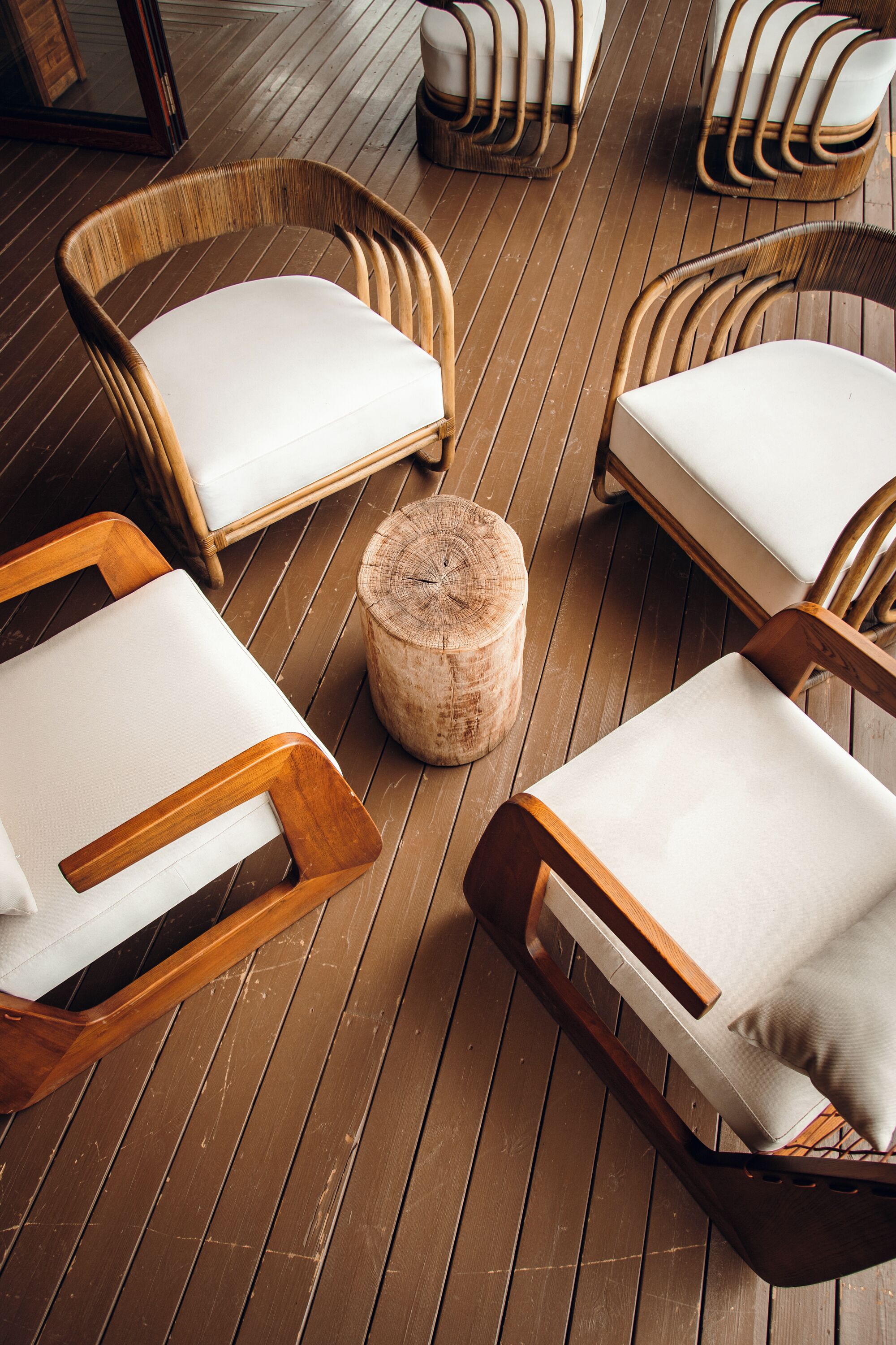 A wooden deck with four wicker lounge chairs and a central round wooden stool.