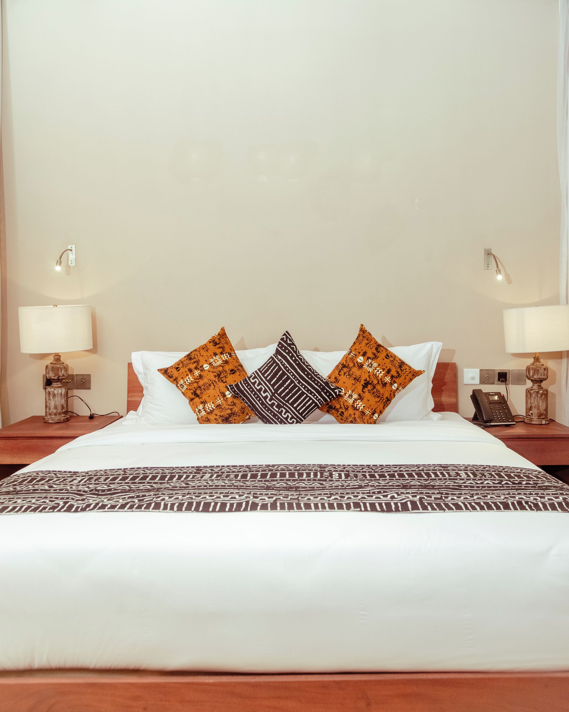 A neatly made bed with white linens and patterned pillows, two bedside lamps, and a telephone on the nightstand.