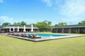 A swimming pool with lounge chairs and umbrellas, surrounded by a grassy area and buildings with green roofs.