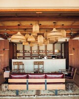 Zona de bar con techo de madera, lámparas colgantes de mimbre, barra con botellas y asientos de cuero.