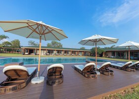 A poolside area with lounge chairs and umbrellas, a swimming pool, and a building with a tiled roof in the background.