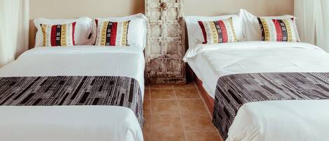 Una habitación con dos camas, cada una con ropa de cama y almohadas estampadas, una pared de ladrillo y una puerta de madera.