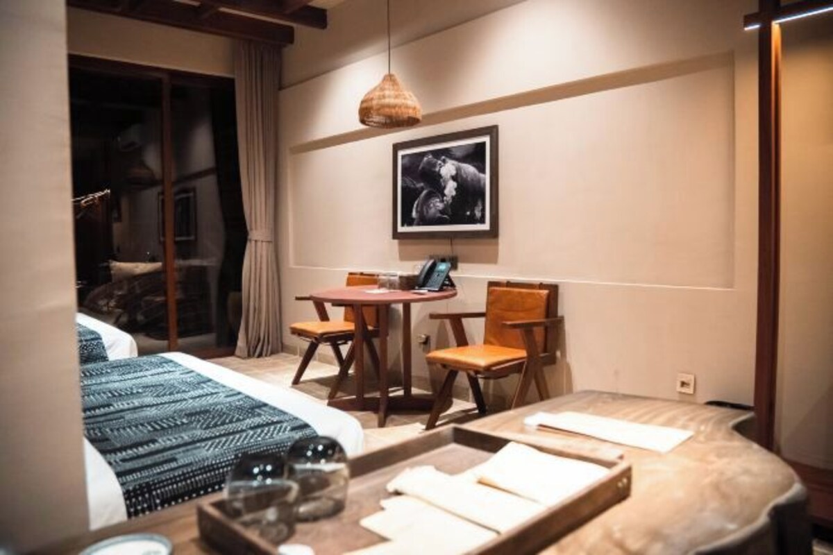 A hotel room with a bed, a dining table with chairs, a small desk with a laptop, and a framed picture on the wall.