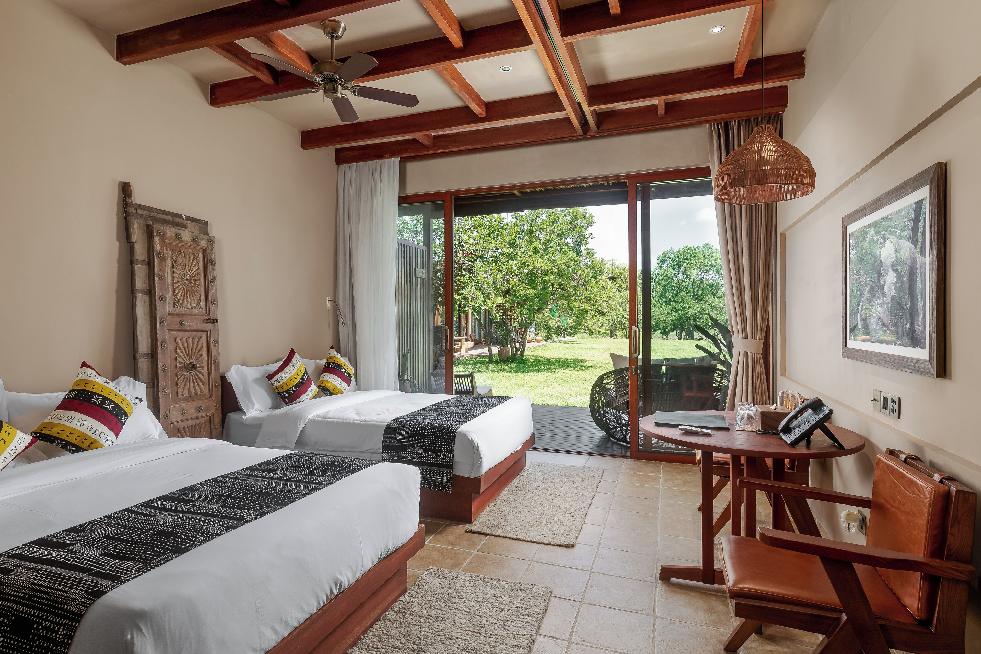 Habitación de hotel con dos camas, zona de comedor y vistas al jardín.