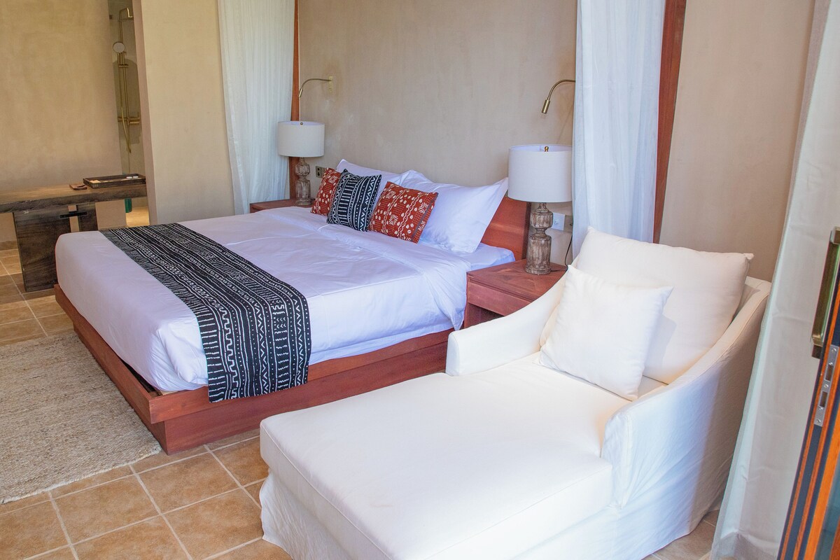 A hotel room with a large bed, a smaller sofa, two bedside lamps, and a nightstand.