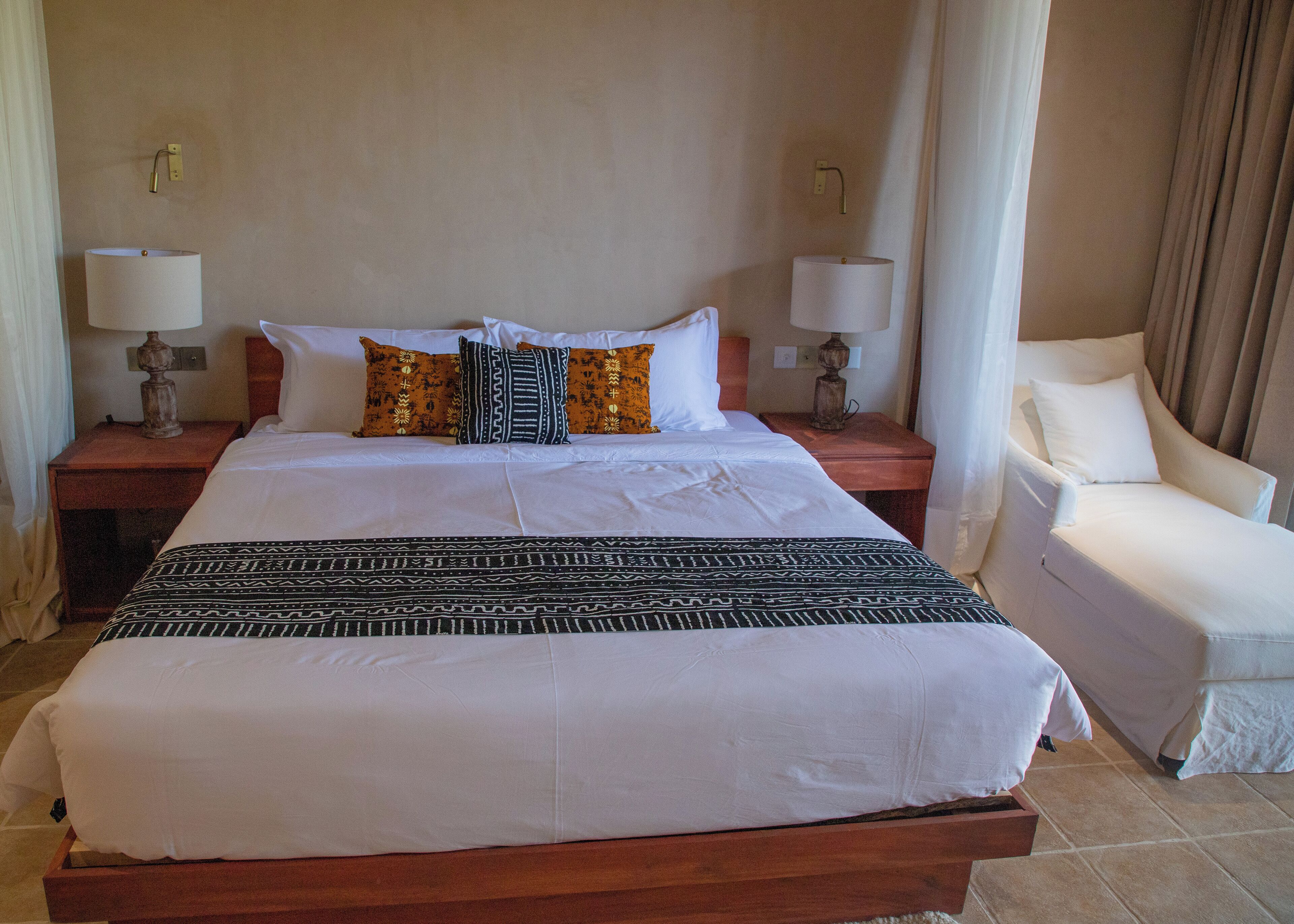 A hotel room with a large bed, two bedside tables with lamps, a chair, and a curtain.