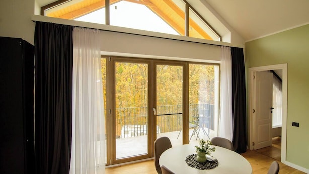 Un espace repas comprenant une table et des chaises, une vue sur les arbres d’automne à travers de grandes portes-fenêtres coulissantes, et un plafond haut avec des poutres en bois.