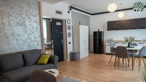 Un salon moderne avec un canapé, un coin repas comprenant une table et des chaises, et une cuisine équipée de placards et d’un plan de travail.