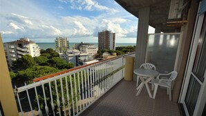 A balcony with a view of the sea and buildings. There are two white chairs and a table. - Stunning sea View From our Apartment With Terrace (Lignano Sabbiadoro)