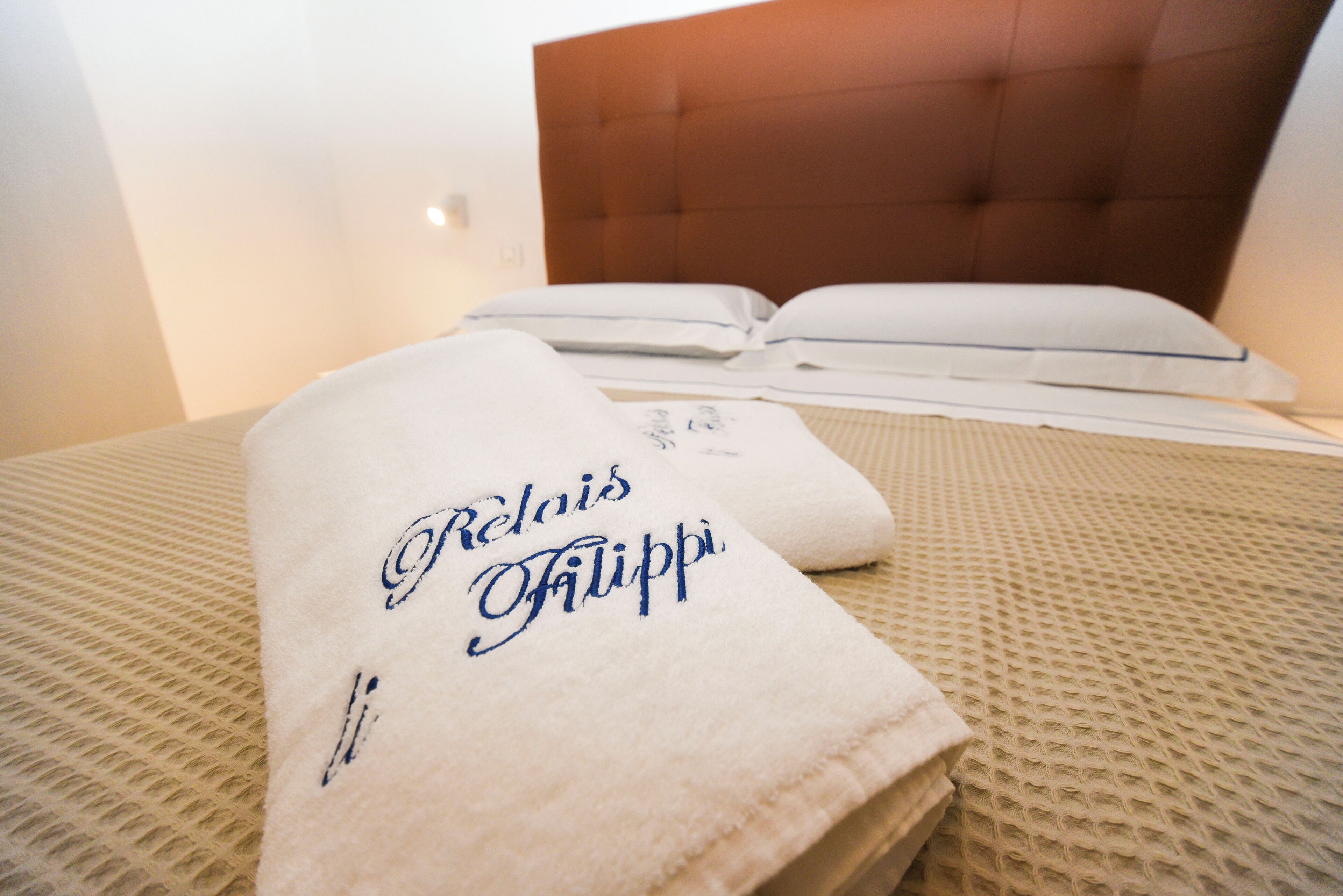 A neatly made bed with a white towel featuring embroidered text, a headboard, and a textured bedspread.