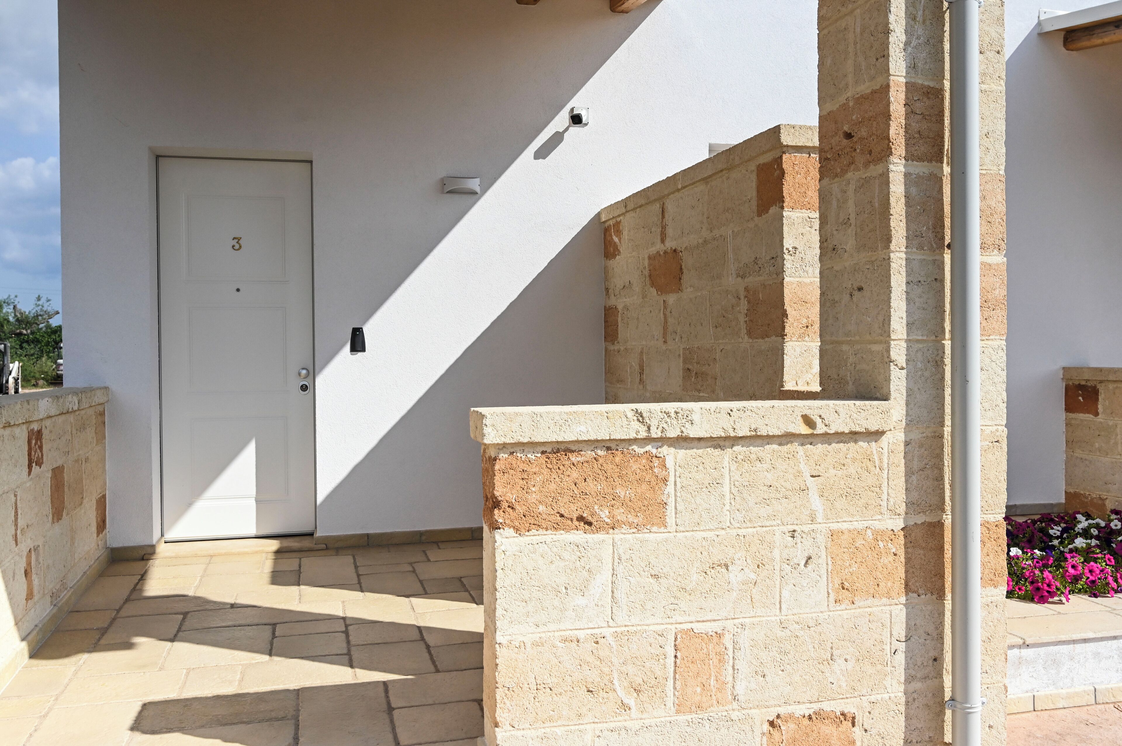 A white door with the number 3, a stone wall, and a tiled patio area.