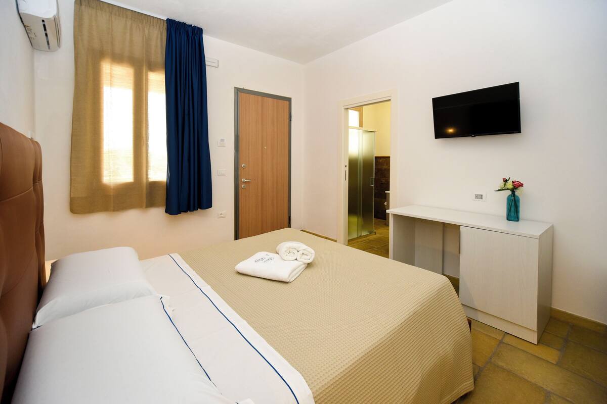 A hotel room with a bed, a desk, a TV, and a bathroom visible through an open door.