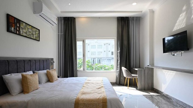 Ein modernes Hotelzimmer mit einem großen Bett, einem Schreibtisch, einem Fernseher und einem Fenster mit Blick auf Gebäude.