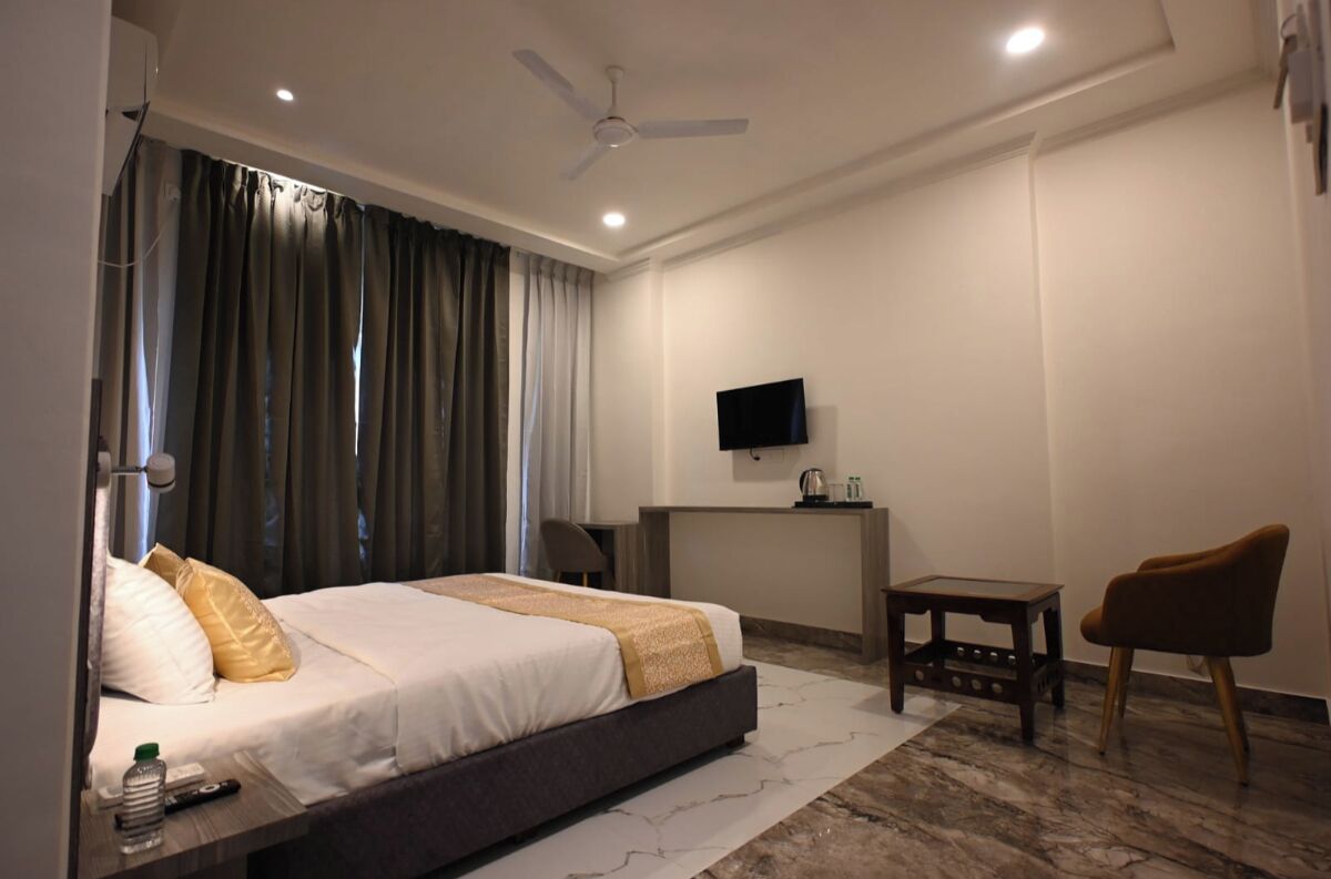 Habitación de hotel con cama, escritorio, silla, televisor y ventilador de techo.